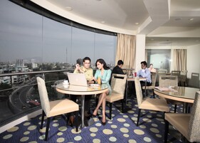 A modern hotel room with a panoramic city view, a round dining table, and comfortable seating.
