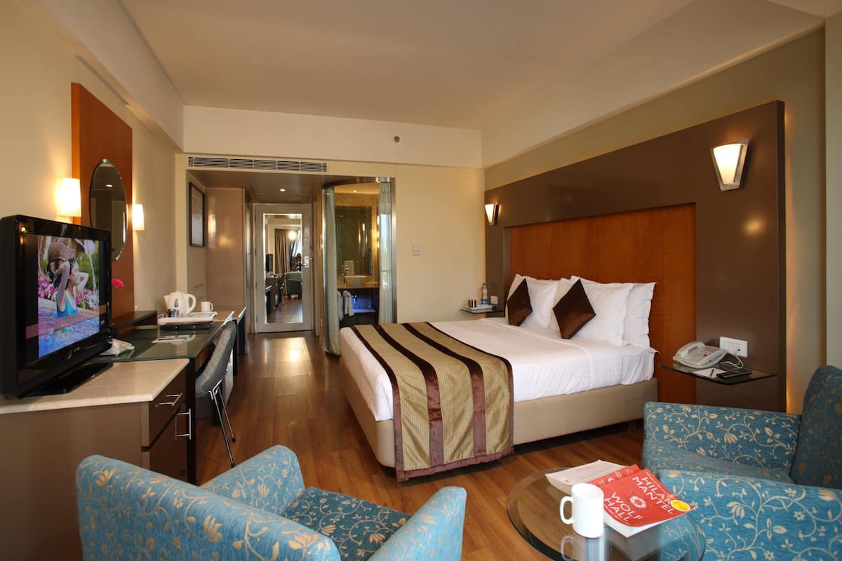 A hotel room with a bed, a TV, a desk, and a seating area.