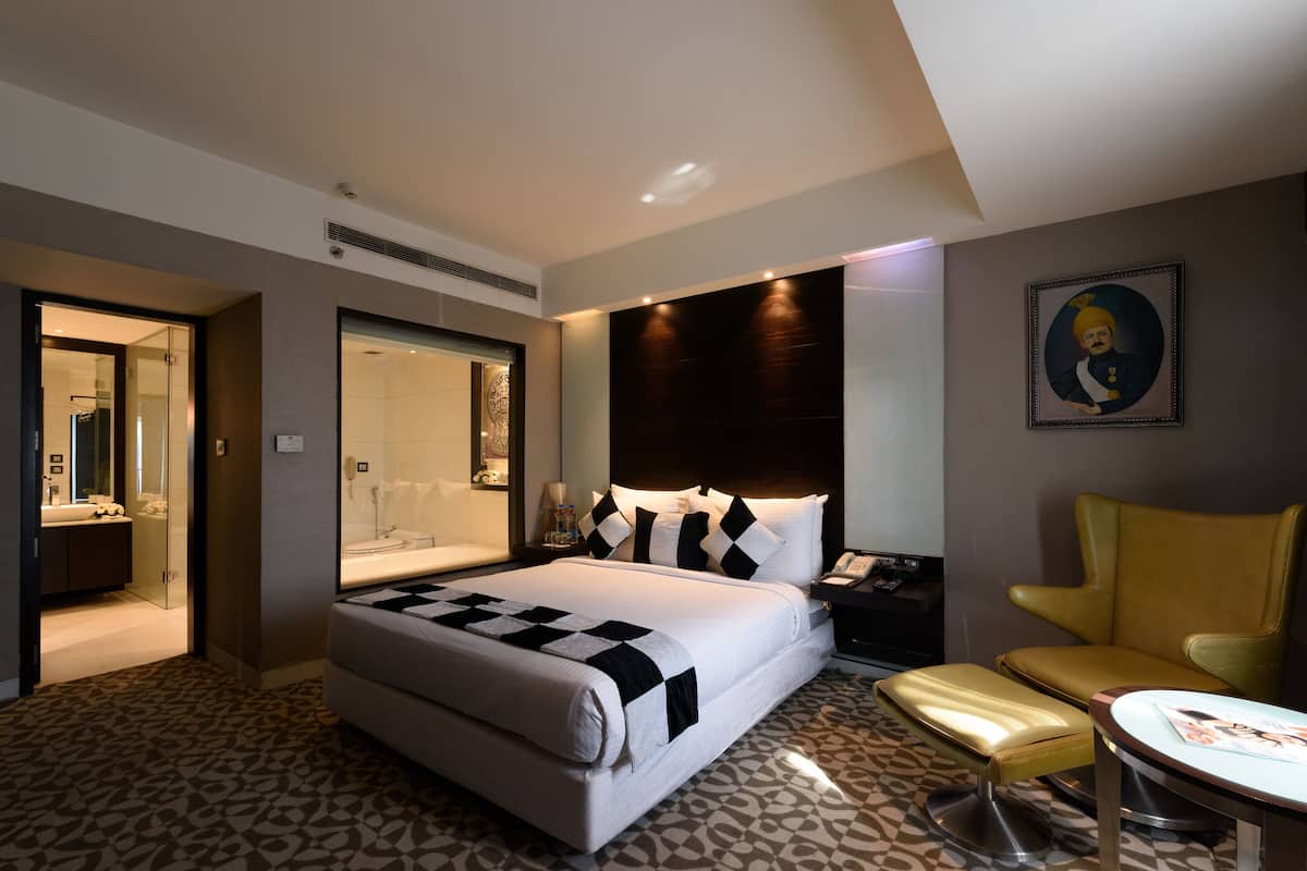 Una habitación de hotel con una cama grande, una mesita de noche, una silla, una pequeña mesa y un baño visible a través de una puerta abierta.