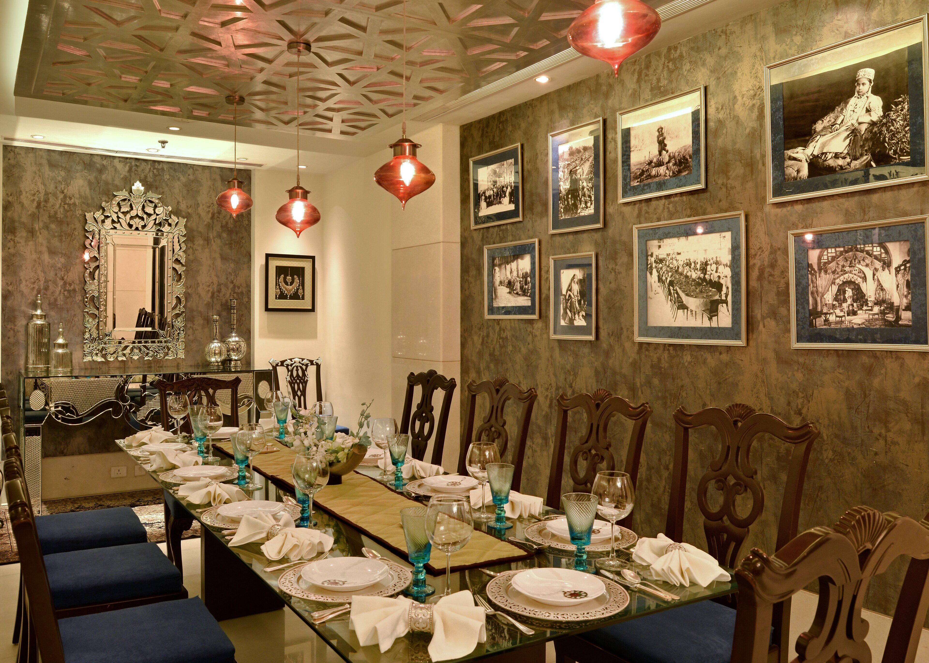 A formal dining room with a long table set for a meal, framed historical photographs on the walls, and ornate ceiling design.