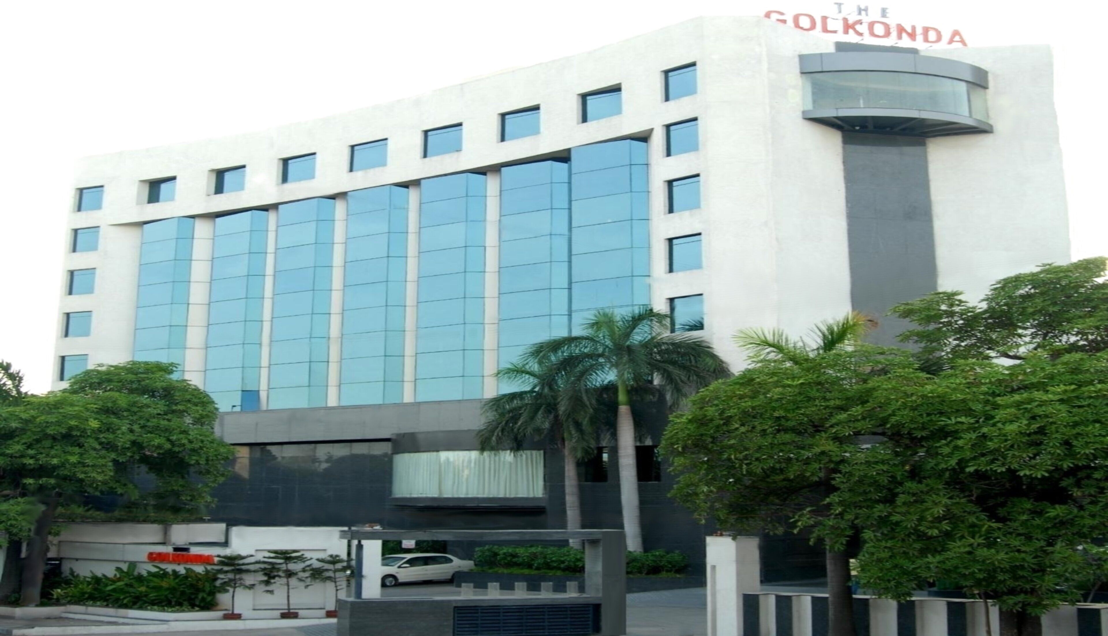 A modern building with a glass facade, a prominent vertical structure on the right, and a car parked in front.