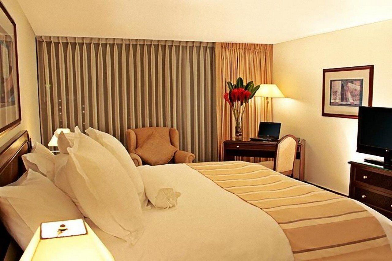A hotel room with a large bed, a chair, a desk with a lamp, and a television.