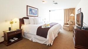 A hotel room with a large bed, a desk with a lamp, a chair, a television, and a window with curtains. - Thunderbird Fiesta Hotel & Casino (Lima)