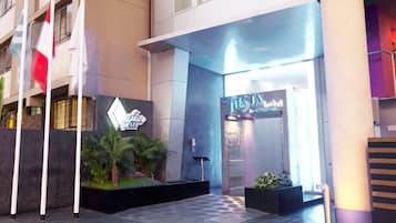 A hotel entrance with a modern design, including a neon sign, a reception desk, and a staircase leading to the entrance.