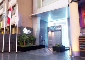 A hotel entrance with a modern design, including a neon sign, a reception desk, and a staircase leading to the entrance.