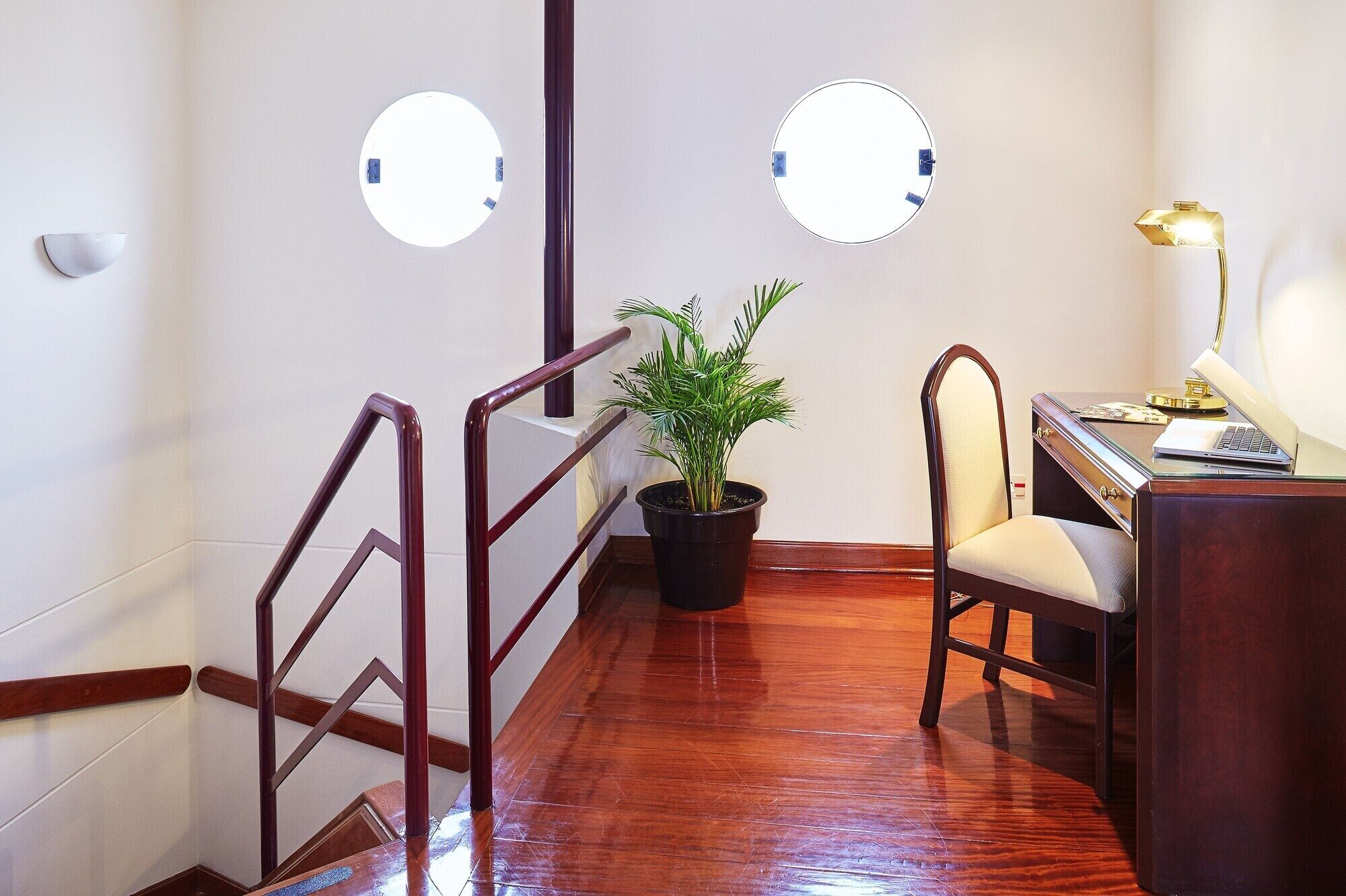 A staircase with wooden railings, a potted plant, a desk with a chair, and two wall-mounted lights.