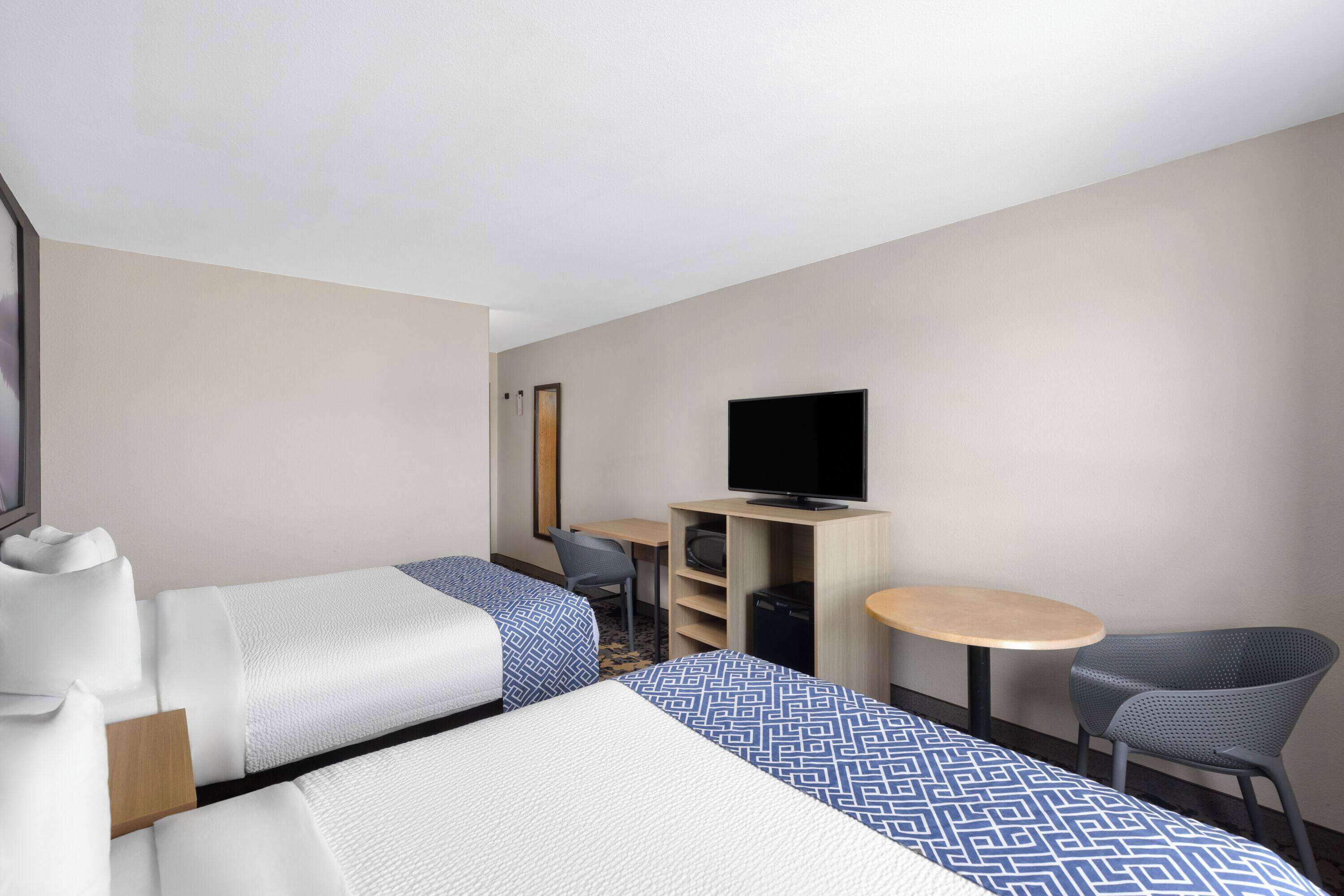 A hotel room with two beds, a television, a small desk, and a chair.