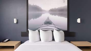 A bedroom with a large framed picture of a kayak on a misty lake, a bed with white bedding, and two bedside tables with lamps.