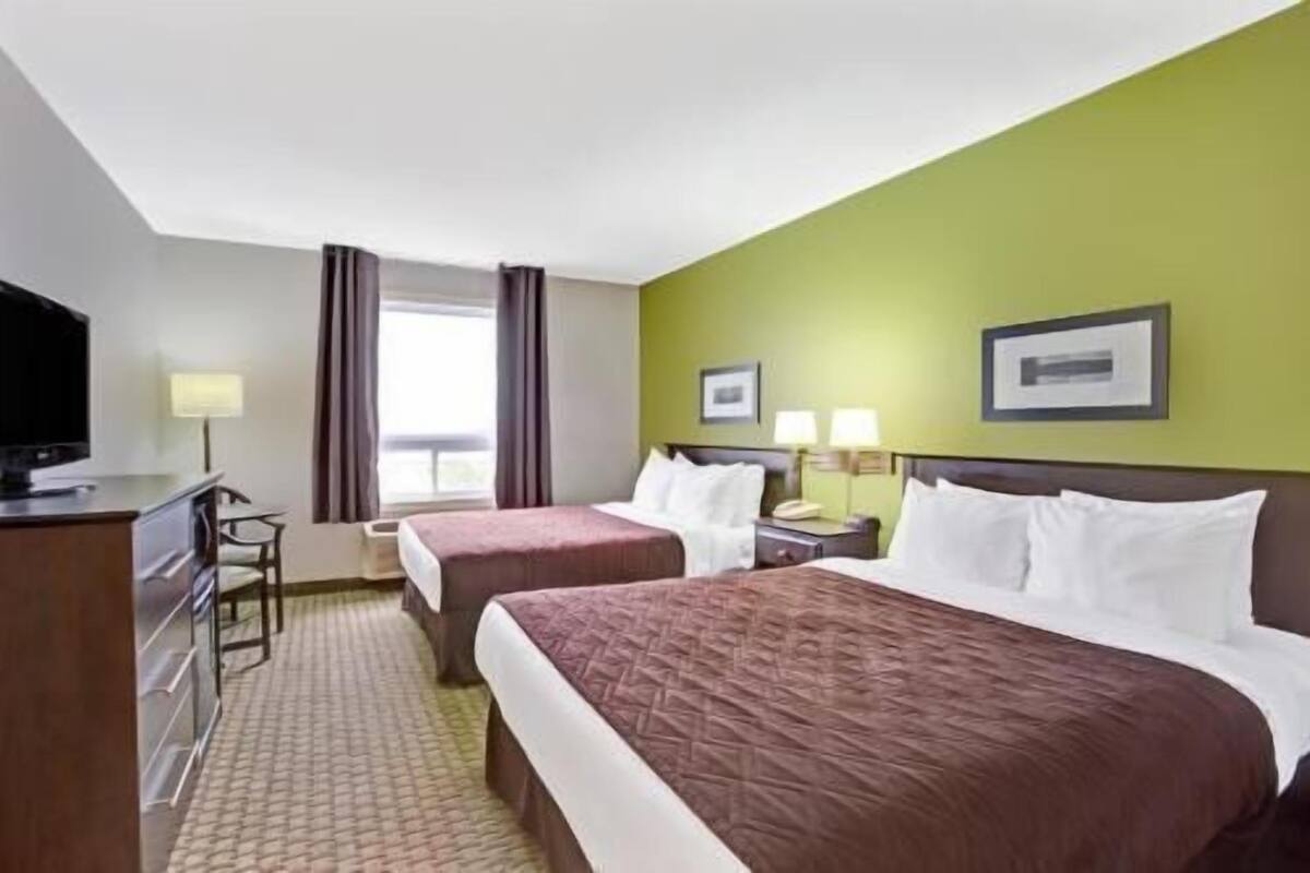 Une chambre d’hôtel avec deux lits, une télévision, un bureau et une fenêtre avec des rideaux.