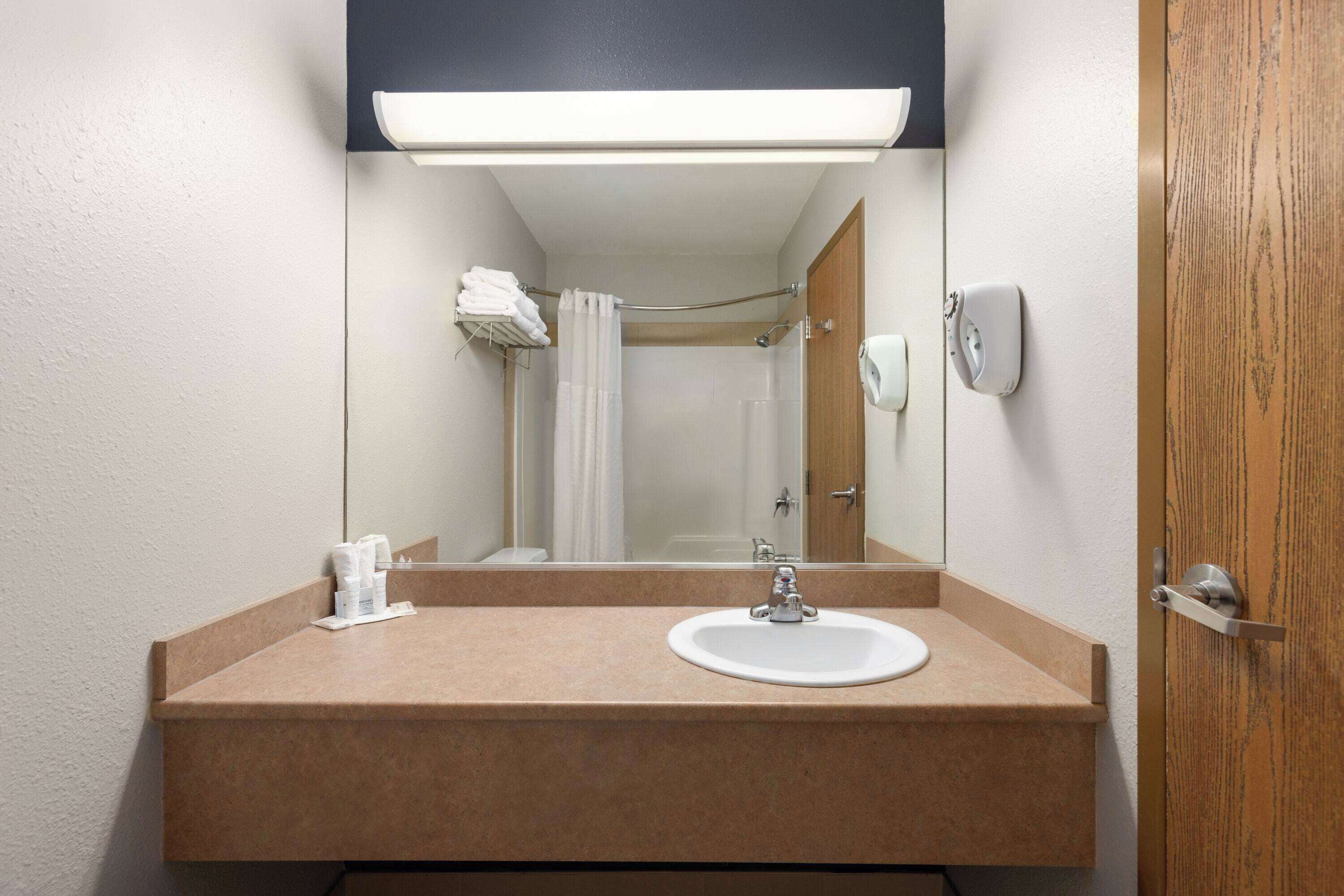 Un baño con lavamanos, espejo, toallero y cortina de ducha.