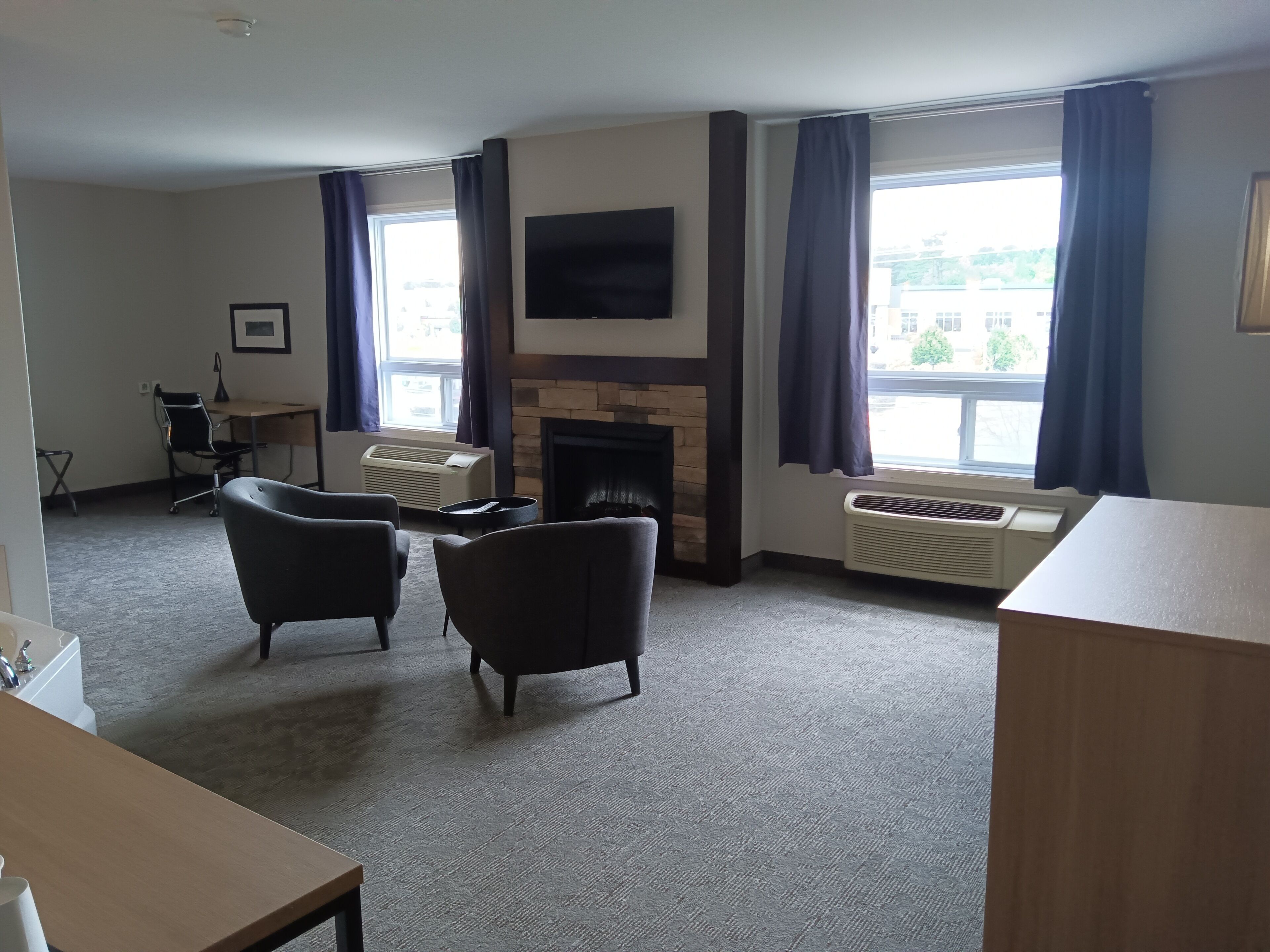 Ein Hotelzimmer mit Kamin, zwei Sesseln, einem Schreibtisch und einem großen Fenster mit Vorhängen.