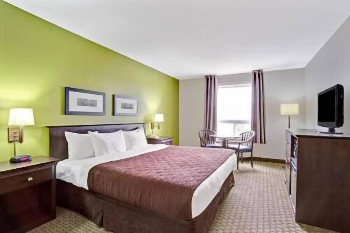 Une chambre d’hôtel comprenant un lit, un bureau avec un ordinateur, deux chaises et un téléviseur.