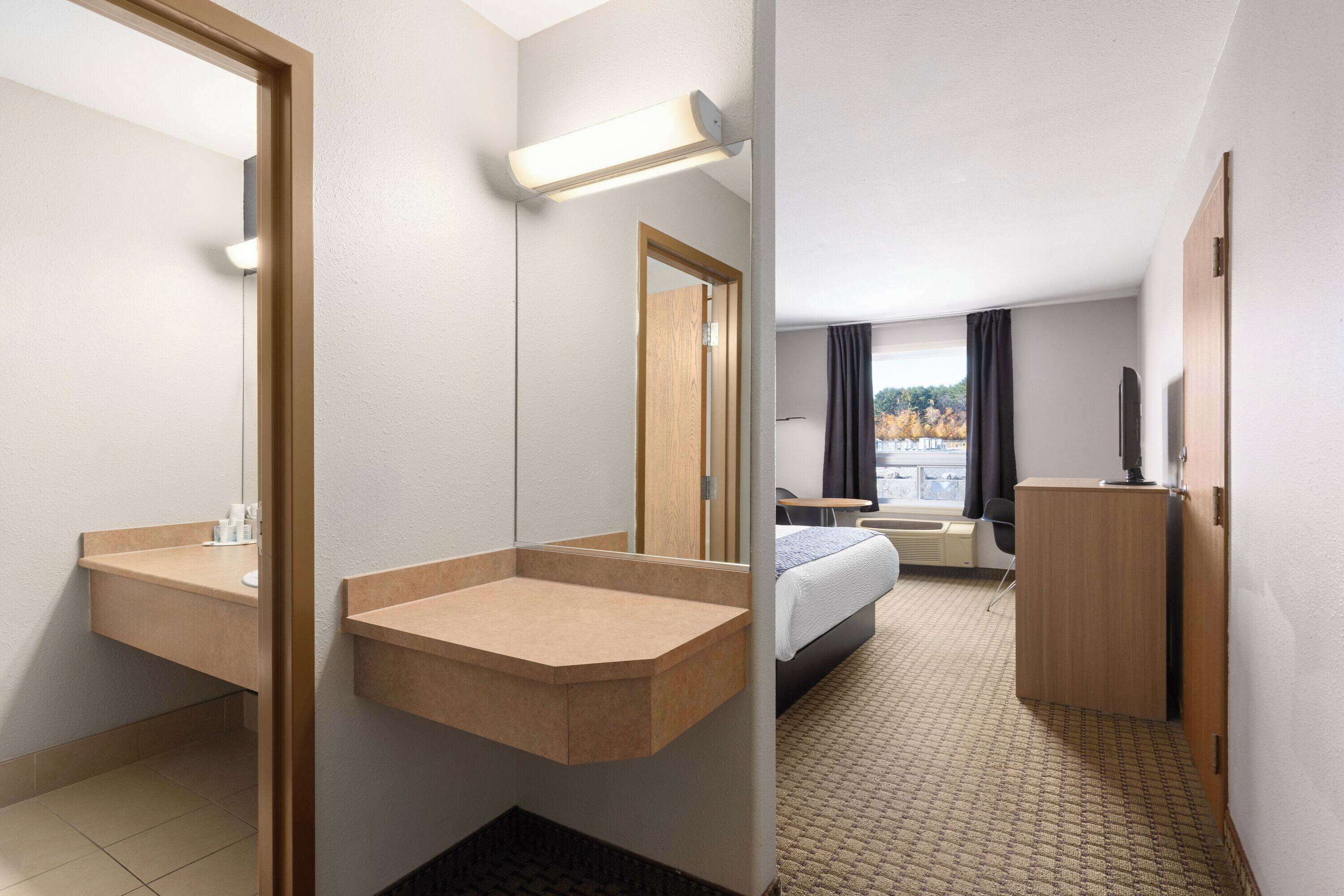 A hotel room with a large mirror, a built-in sink, a bed, a wardrobe, and a view of the outdoors.