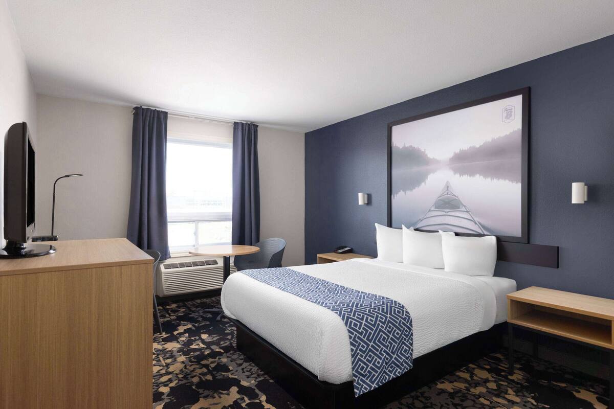Une chambre d’hôtel avec un grand lit, un bureau, une chaise, une petite table et un tableau au mur.