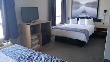 A hotel room with a bed, a TV on a wooden cabinet, a large painting on the wall, and a window with curtains.