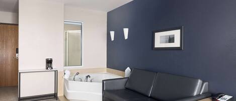 A modern bathroom with a bathtub, a black leather sofa, and a small wooden table with a phone.