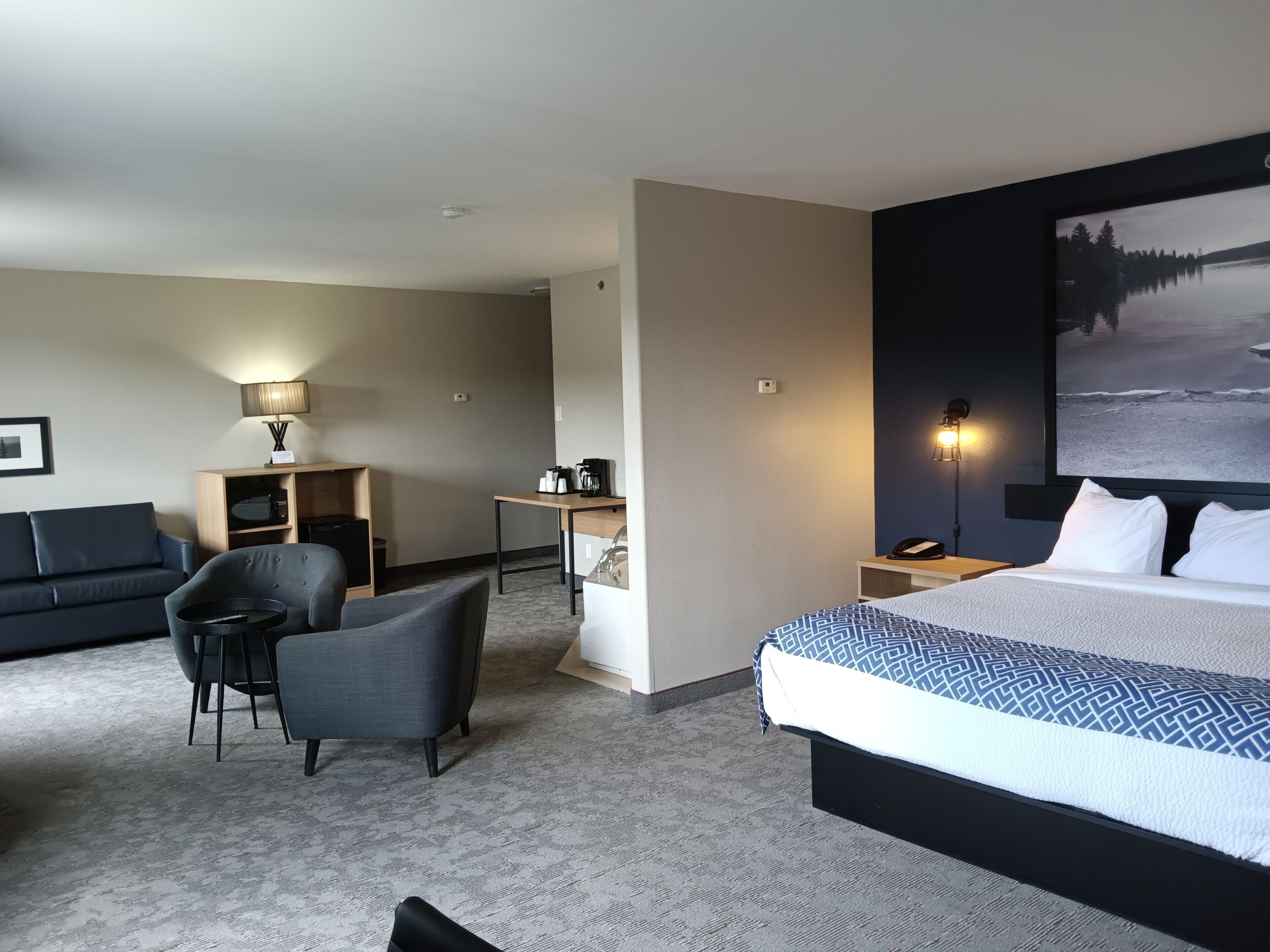 A hotel room with a bed, a desk, a chair, a sofa, and a wall-mounted TV.