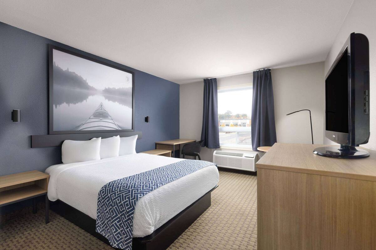 Une chambre d’hôtel avec un grand lit, un bureau, une chaise, une télévision et une fenêtre avec des rideaux.