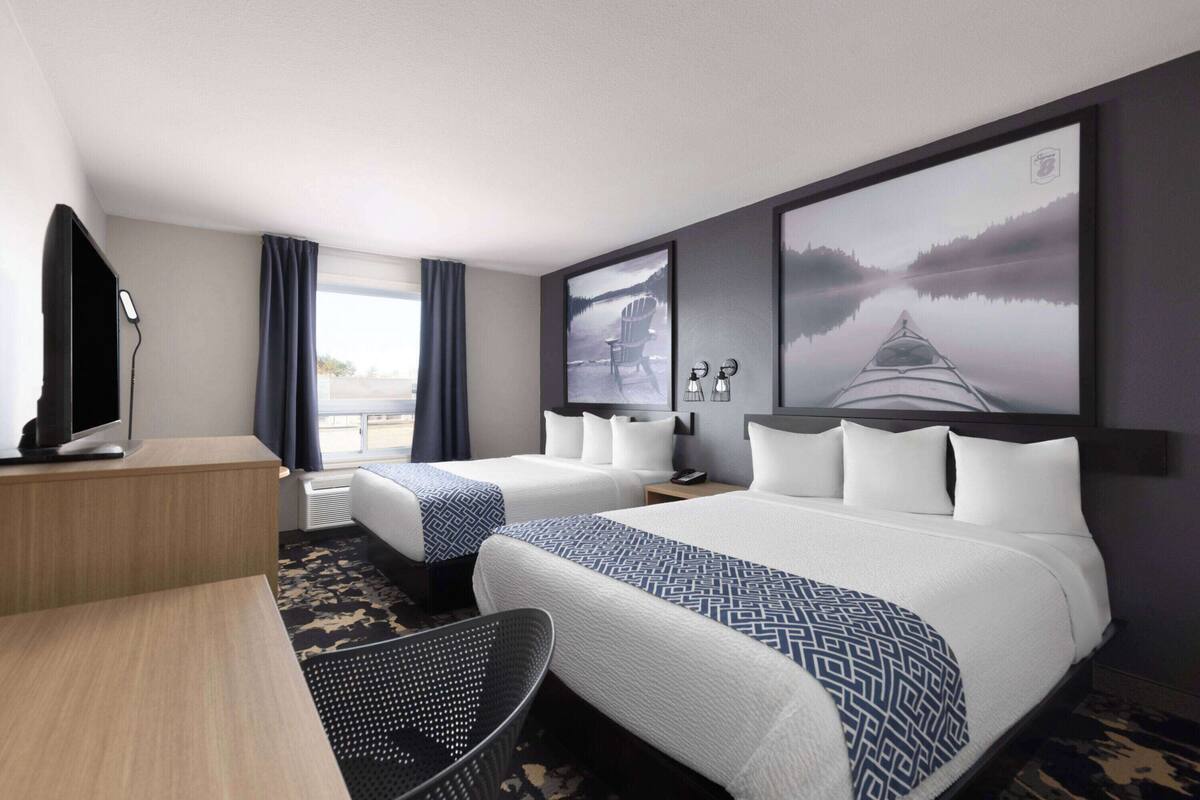 Une chambre d’hôtel avec deux lits, un bureau, une chaise, une télévision et des œuvres d’art accrochées aux murs.