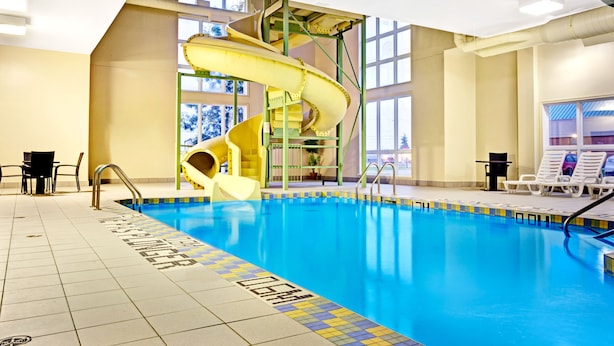 Una piscina interior con un tobogán amarillo, zona de piscina despejada y ventanas iluminadas por el sol.