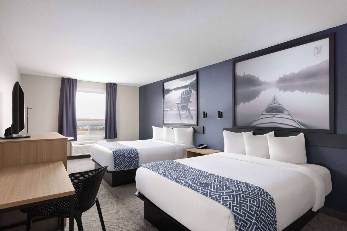 Une chambre d’hôtel avec deux lits, un bureau, une chaise et de grandes images encadrées accrochées aux murs.