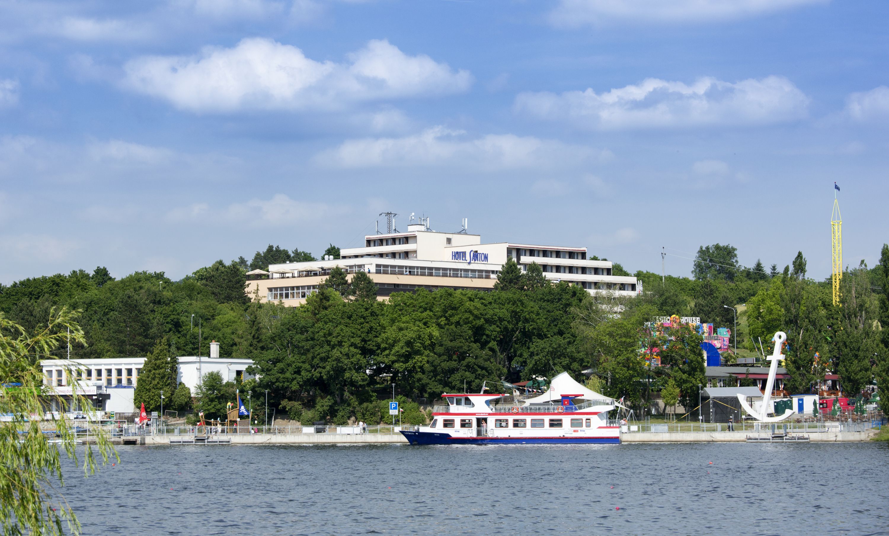 A hotel with multiple floors, a boat docked nearby, and a large white tower in the background.