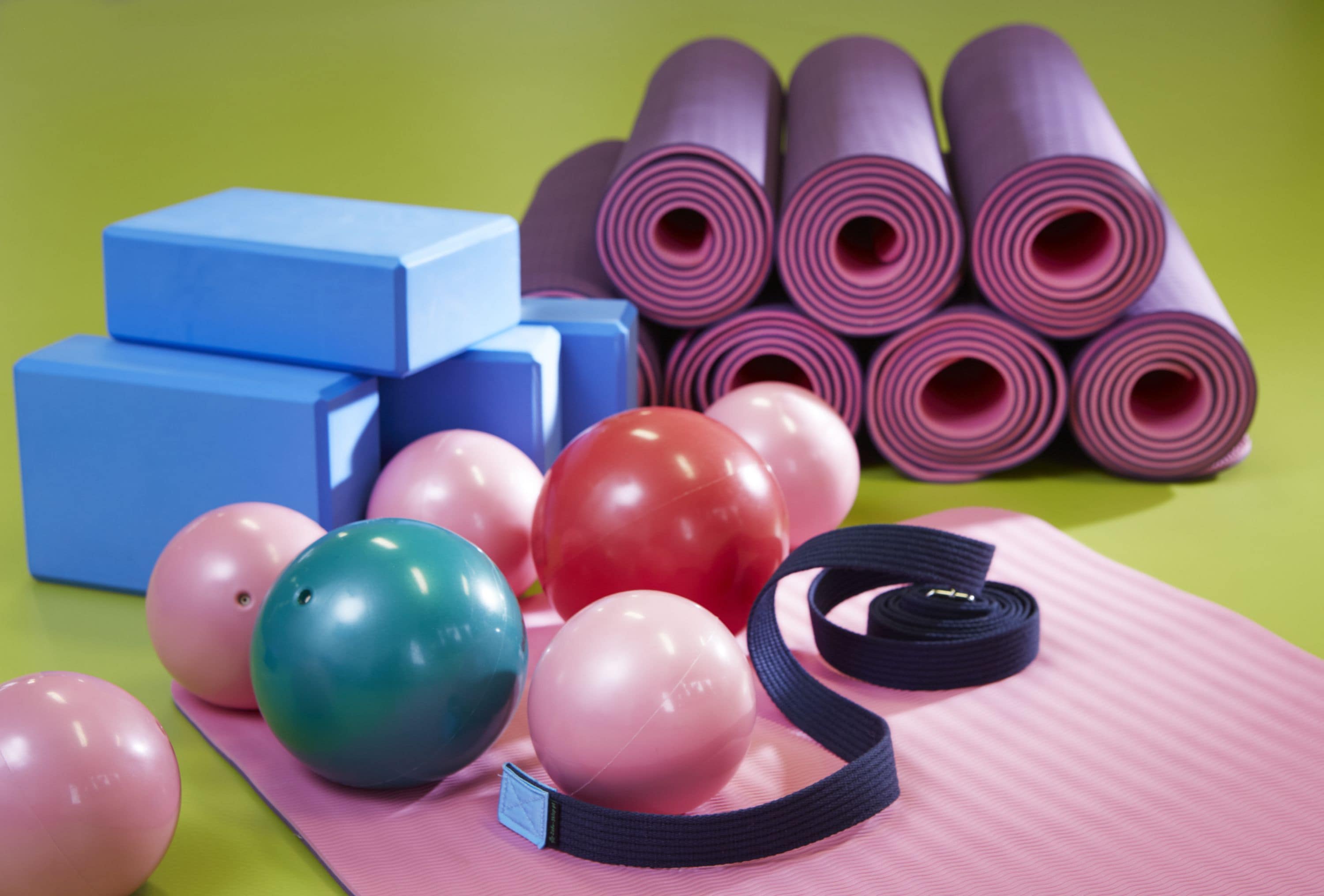 A collection of exercise equipment including yoga mats, foam blocks, and exercise balls on a green surface.