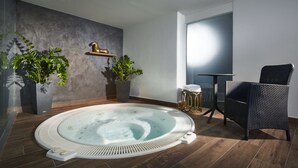 Een moderne badkamer met een vrijstaand bad, twee potplanten, een klein rond tafeltje met een stoel, en een decoratief paardbeeld aan de muur.