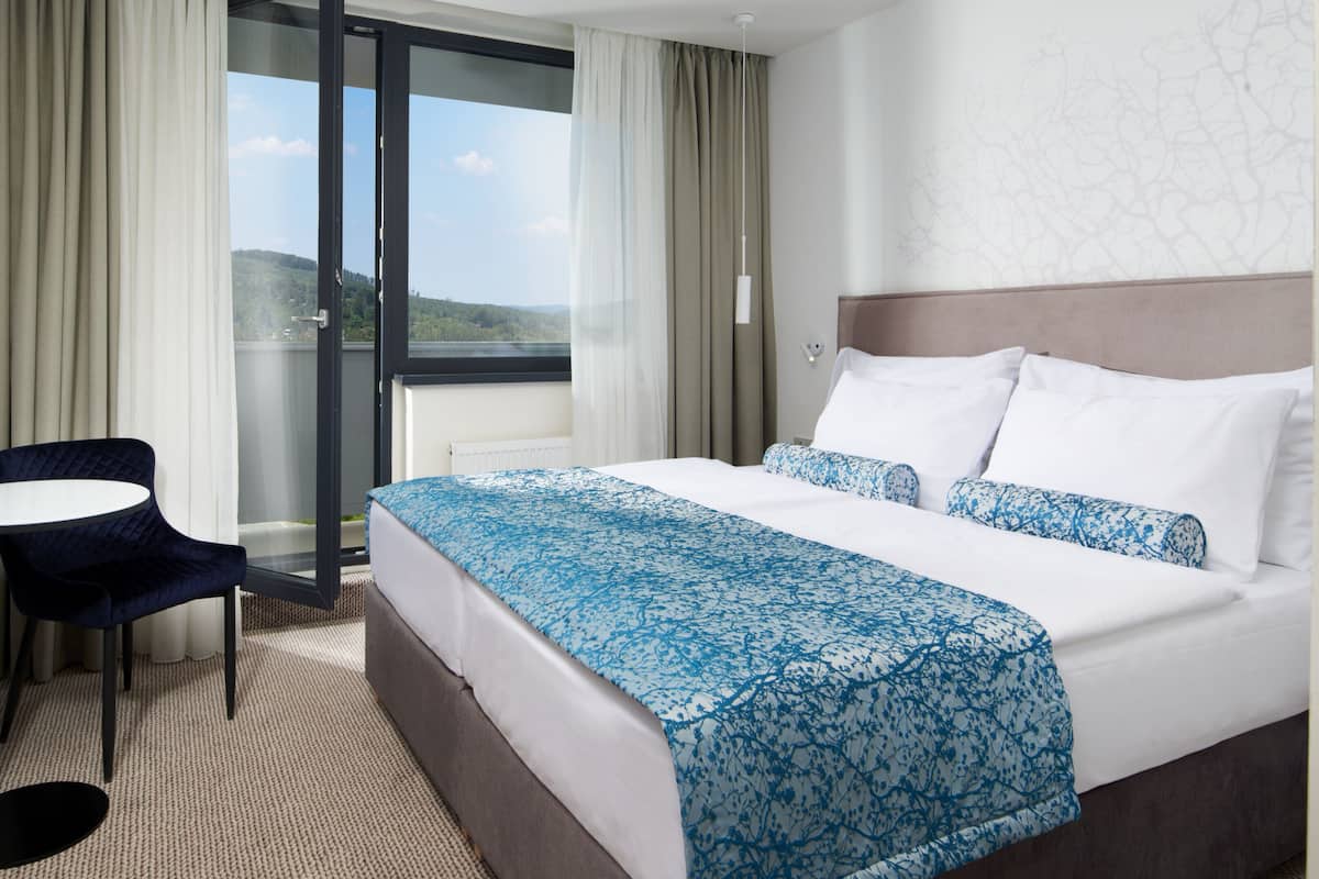 Habitación de hotel con cama, una mesita, una silla, televisión y vistas al exterior.