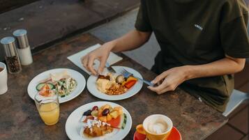 A person sitting at an outdoor table with various food items and a cup of coffee.