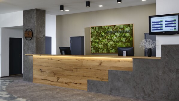 A reception desk with a wooden counter, a large moss wall, and a digital screen displaying conference room information. - Orea Resort Santon Brno (Brno)