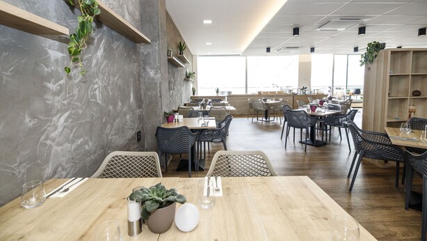 A modern restaurant interior with wooden tables, black wicker chairs, and green plants. - Orea Resort Santon Brno (Brno)
