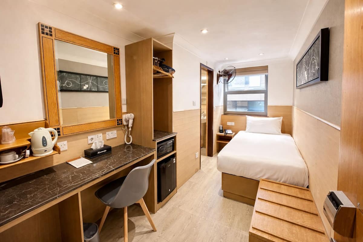 A compact hotel room with a bed, a desk with a telephone, a mirror, and a window.