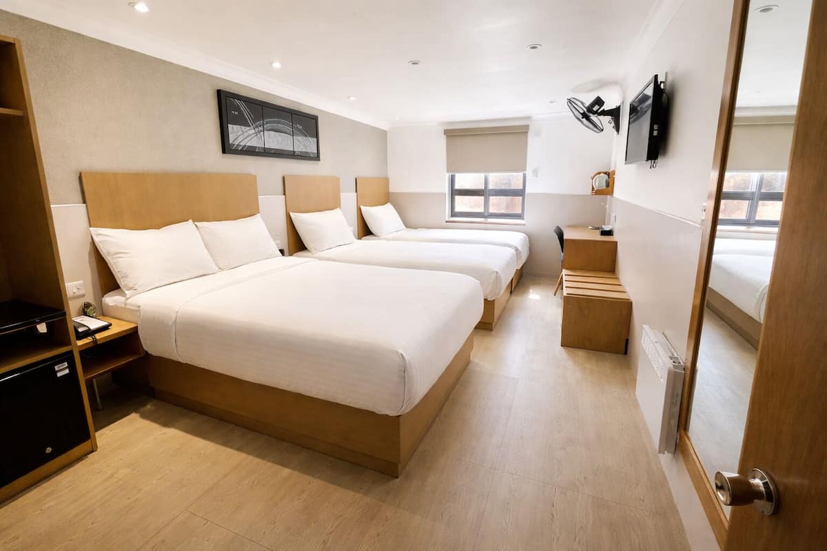 A hotel room with two beds, a desk, a TV, and a window.