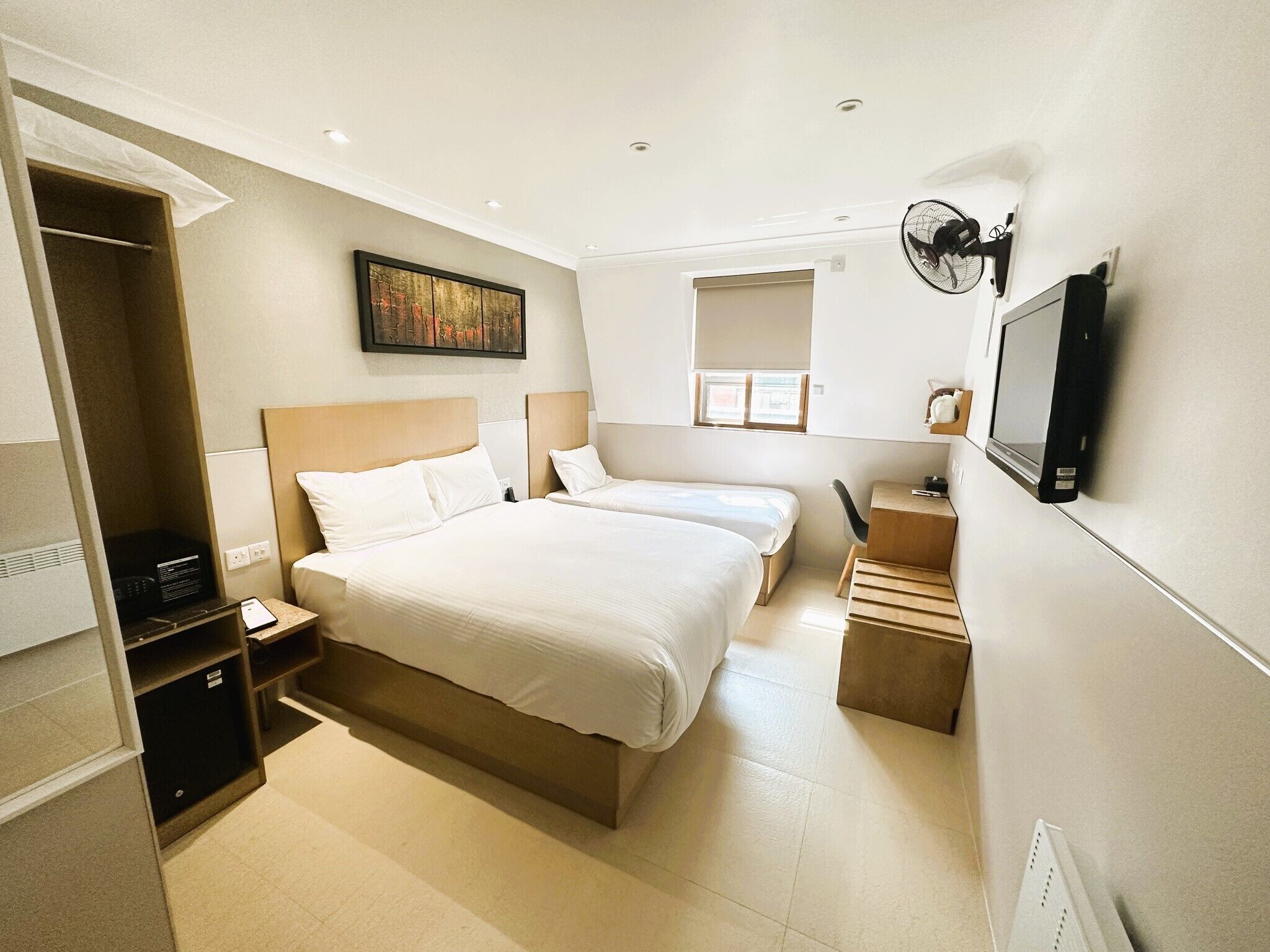 Habitación de hotel con dos camas, un escritorio, una silla, un televisor, un ventilador y una ventana.