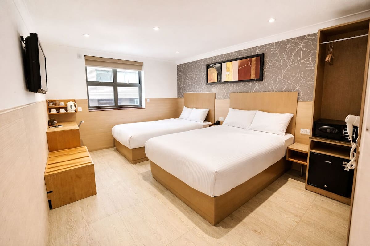 A hotel room with two beds, a wooden wardrobe, a small desk with a kettle, a microwave, and a telephone.