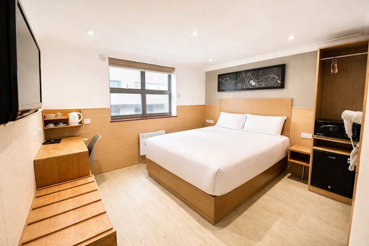 A hotel room with a bed, a desk, a chair, a window, a microwave, and a telephone.