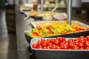 A buffet with various food items including a tray of cherry tomatoes and a colorful vegetable salad. - Heide Park Abenteuerhotel (Soltau)