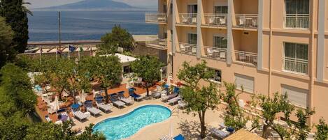 A hotel with a swimming pool, lounge chairs, and a view of the sea.