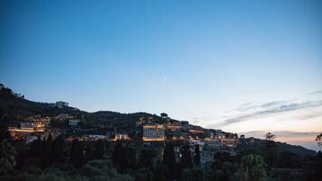 Une ville côtière au crépuscule, avec des bâtiments sur une colline, une lune en croissant dans le ciel et une vue sur la mer.