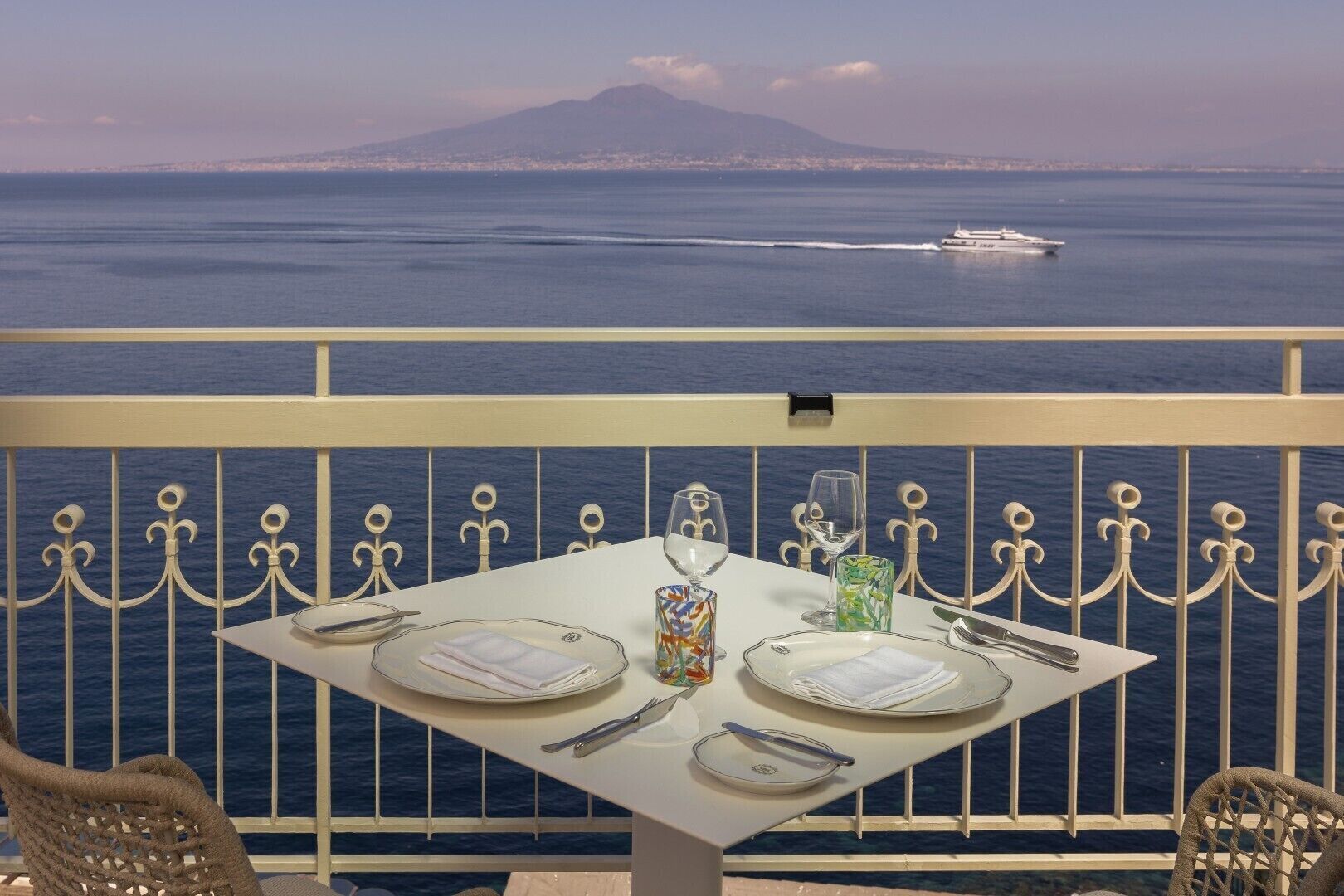 Une table dressée pour deux personnes, avec vue sur la mer et sur une montagne lointaine.