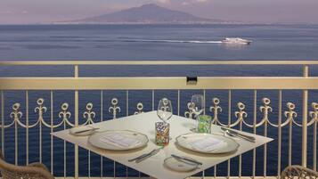 Une table dressée pour deux personnes, avec vue sur la mer et sur une montagne lointaine.