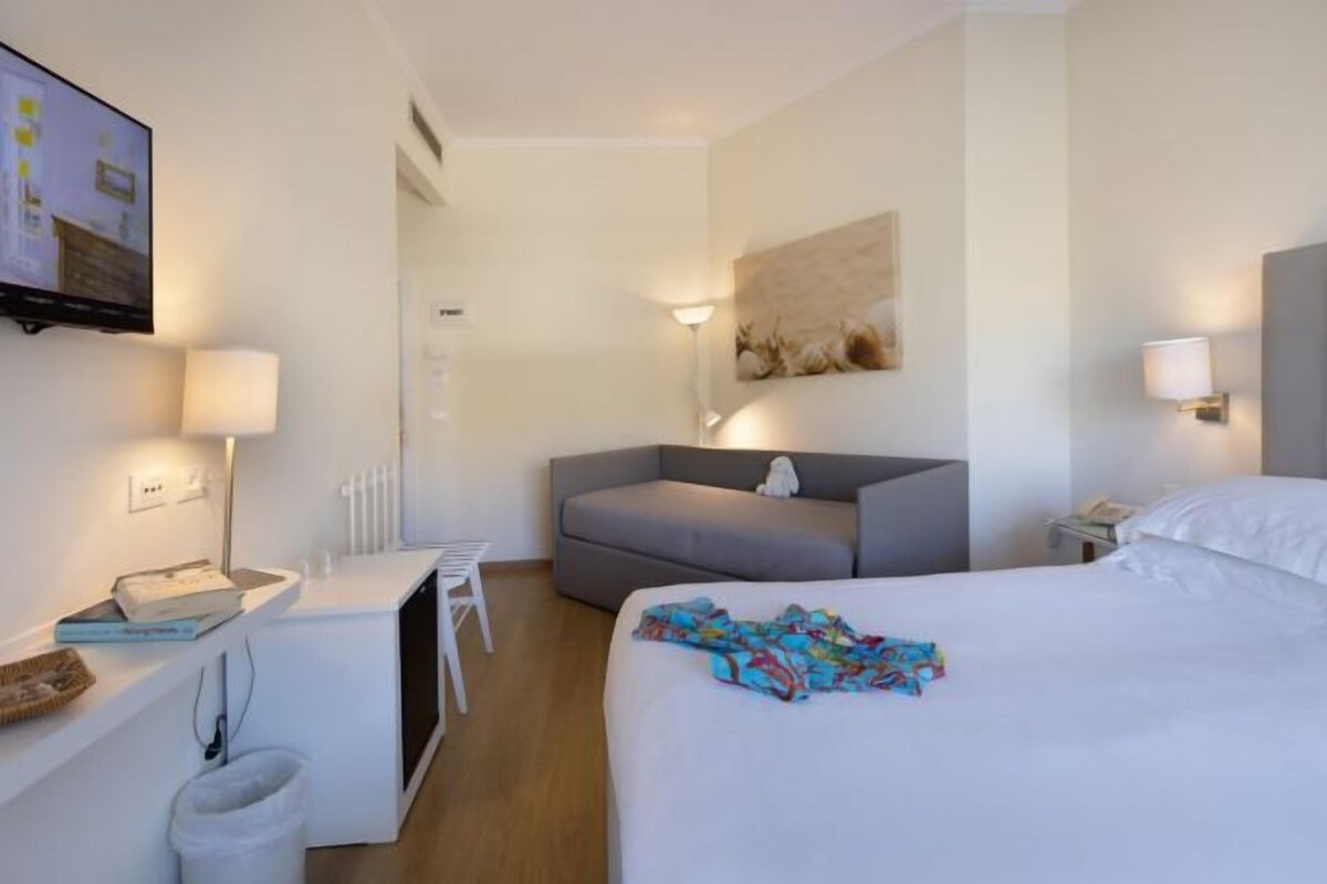Ein Hotelzimmer mit einem Bett, einem Schreibtisch, einem Sessel, einer Couch und einem an der Wand befestigten Fernseher.