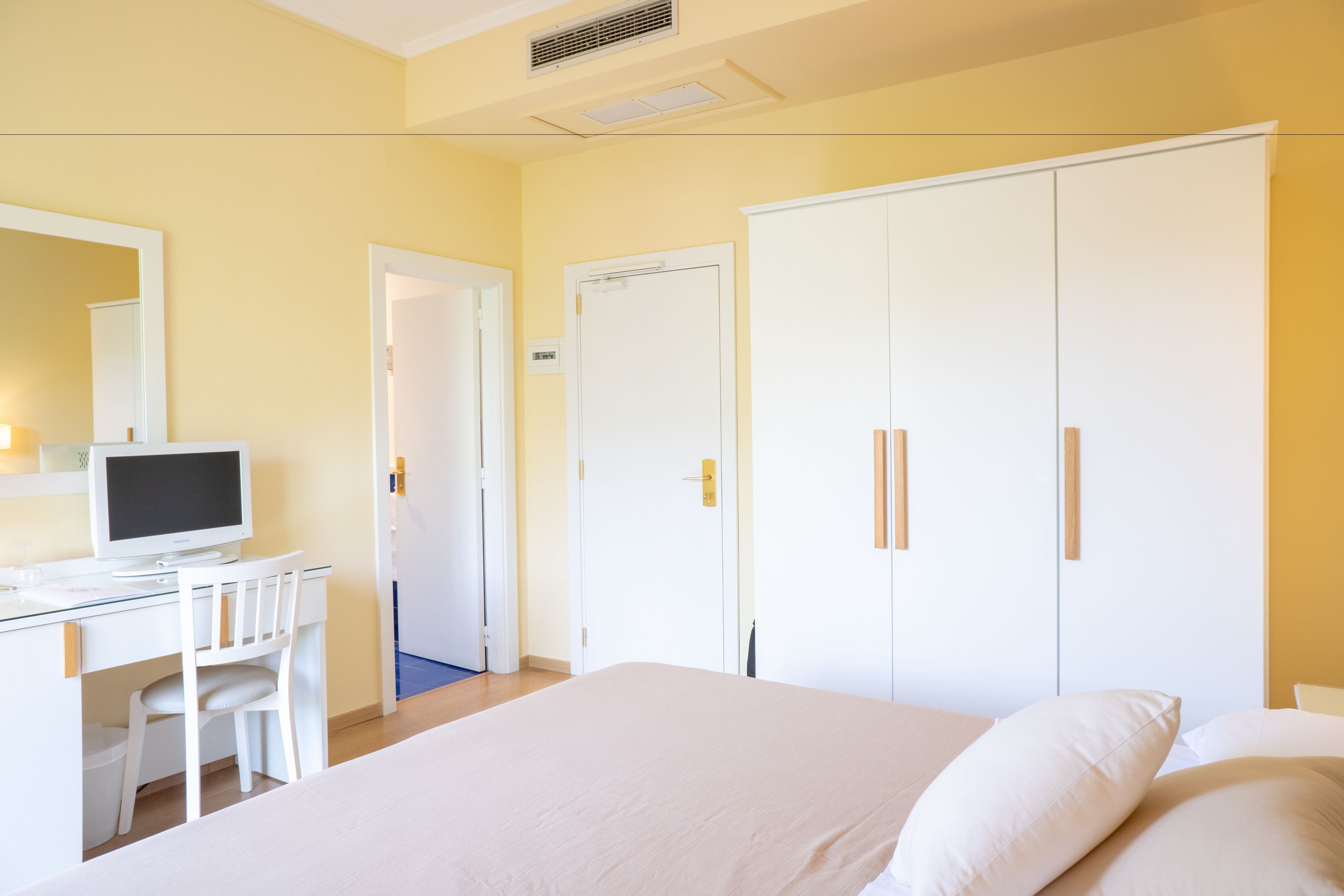 Una habitación de hotel con cama, escritorio con computadora y armario.