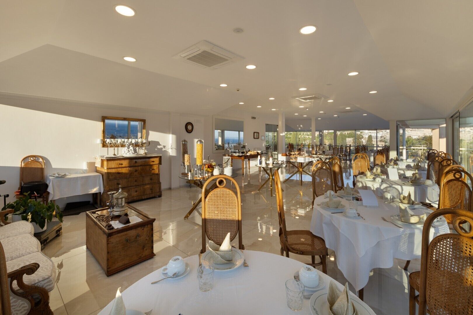 A spacious dining area with round tables, wicker chairs, and a view through large windows.
