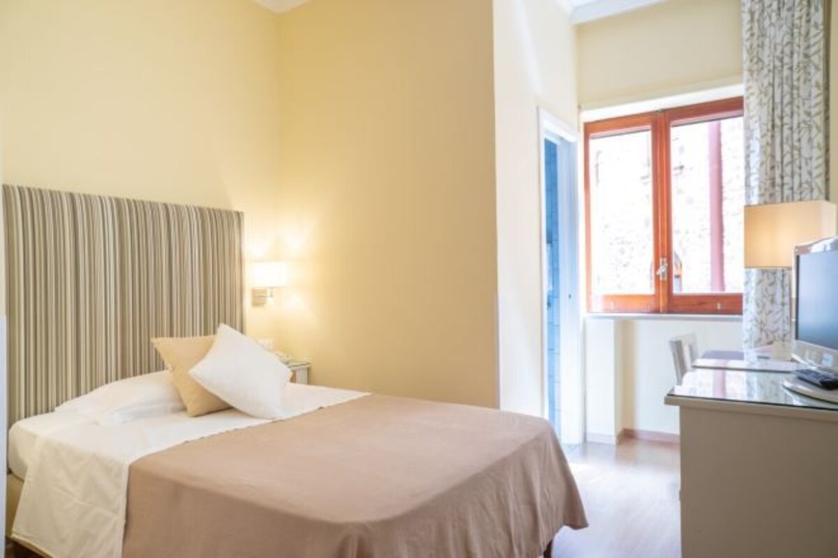 Une chambre d’hôtel avec un lit, une lampe de chevet, un bureau et une fenêtre.
