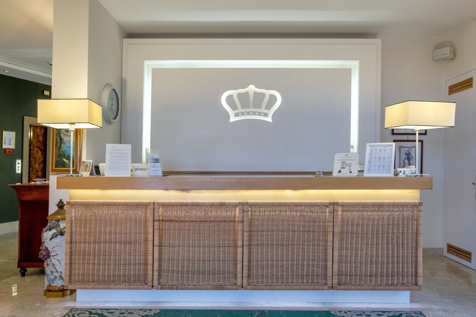 A reception desk with a crown emblem, two lamps, framed certificates, and a clock on the wall.