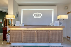 A reception desk with a crown emblem, two lamps, framed certificates, and a clock on the wall. - Hotel Regina Sorrento (Sorrento)