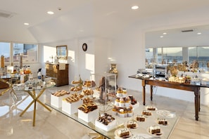 A spacious room with a large dining table displaying various desserts, a wooden cabinet, and a large window offering a view.