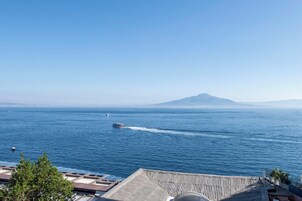 A coastal view with a boat on the water, a mountain in the distance, and a building with a sloped roof.